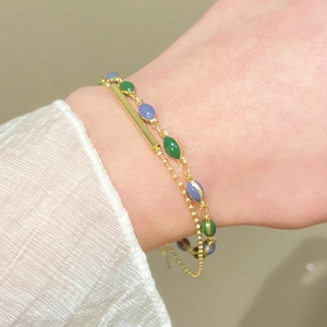 Dettaglio di un bracciale dorato a doppio strato con perline verdi e blu sul polso