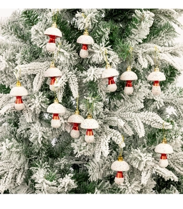 Detail of red and white mushroom ornaments with gold strings hanging on a snowy Christmas tree
