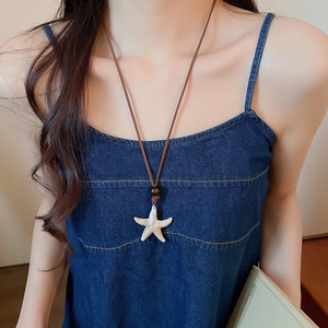Detailed view of white starfish pendant with leather cord on model neck for beach style