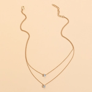 Double layered gold necklace with teardrop zircon pendants on a warm peach background