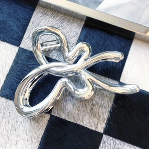 Silver metallic shark hair claw clip with irregular sleek lines on checkered background