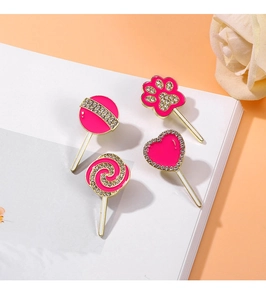 Close-up of four pink enamel pins including a lollipop and paw print on a white book