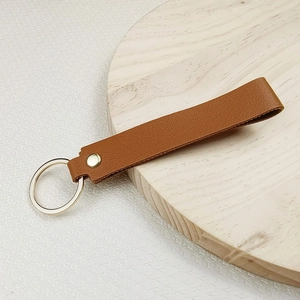 Brown leather keychain wristlet with silver metal ring and golden rivet on wooden display