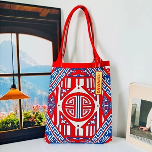 Close-up of knit tote bag featuring red white blue geometric patterns and a red shoulder strap