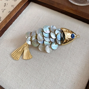 Detail of fish-shaped hair clip with shimmering shell scales and blue evil eye accent
