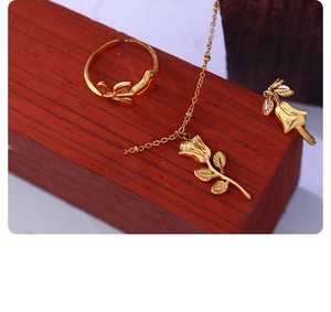 Detailed view of a gold rose pendant necklace and leaf ring set on a red base
