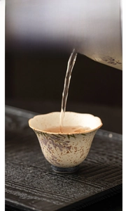 Detail showing the pouring of tea into a wisteria ceramic cup with a wavy gold rim
