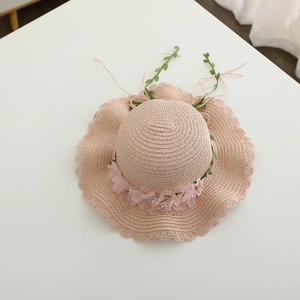 Detailed view of woven pink straw hat with chiffon floral trim and green leaf ribbon