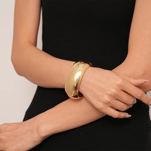 Polished gold metallic wide cuff bracelet with mirror finish on model wearing black clothes