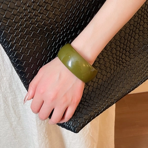 Detail view of a wide olive green acrylic bangle with a smooth polished finish on a model