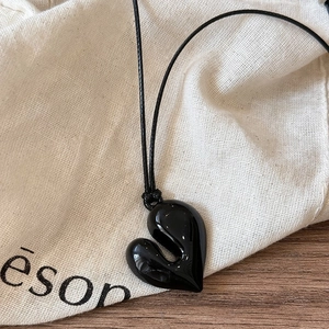 Dettaglio di un ciondolo a cuore nero minimalista in resina liscia su tavolo di legno