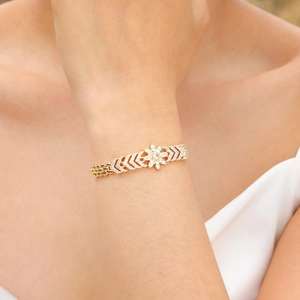 Close-up of golden floral bracelet with sparkling zircon on model's wrist outdoors