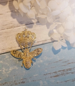 Broche abeille et couronne dorée avec cristaux et perle sur fond de bois bleu