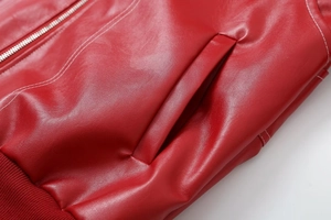 Close-up of red leather jacket featuring zipper detail, white stitching, and ribbed hem