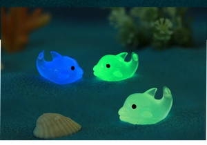 Macro shot of luminous resin dolphins glowing in green and blue on blue sand