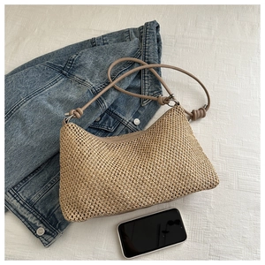 Top-down view of hand-woven straw tote bag with knot strap detail on white knit fabric