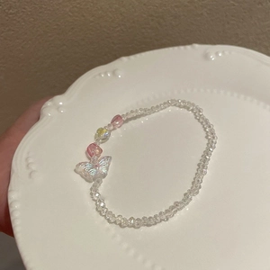 Close-up of beaded bracelet with iridescent butterfly charm and heart beads on white plate