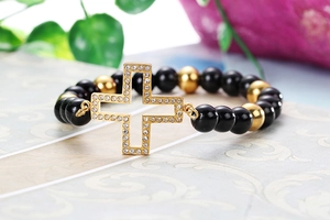Close-up of black and gold beaded bracelet featuring a sparkling rhinestone cross charm