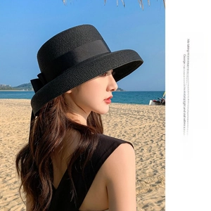 Detail of wide brim straw sun hat with large black bow ribbon against beach backdrop