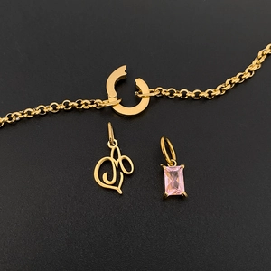 Detail of gold-plated titanium steel bracelet with letter M and pink gemstone charms