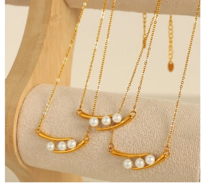 Détail d'un collier doré élégant avec pendentif incurvé serti de trois perles blanches