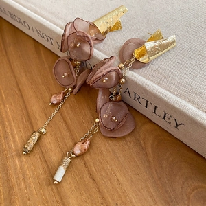 Detail of organza floral earrings with gold chain on a wooden desk with a warm artistic vibe