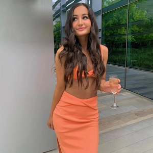 Detail of orange two-piece set featuring twist-front crop top and side slit skirt