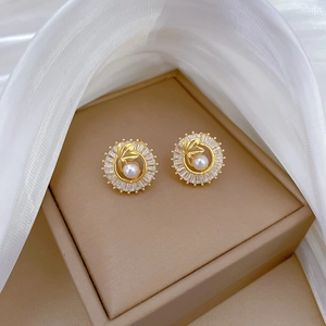 Close-up of golden leaf earrings with white pearls and zircons on a jewelry box