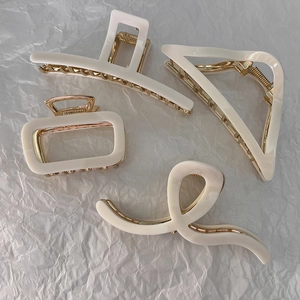 Detail of four cream hair claws with golden metal springs and various geometric shapes