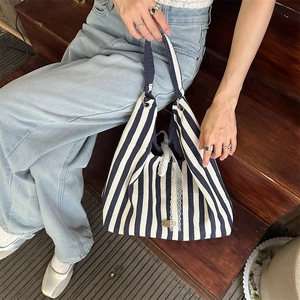 Détail du sac cabas en toile à rayures bleues et blanches avec dentelle et logo en métal
