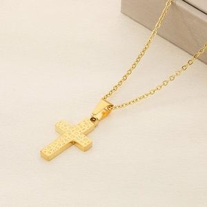 Close-up of golden cross necklace with hammered texture on a neutral fabric background