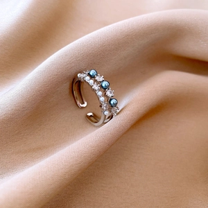 Detail van zilveren open ring met blauwe en witte kralen en zirkoon op zijden stof