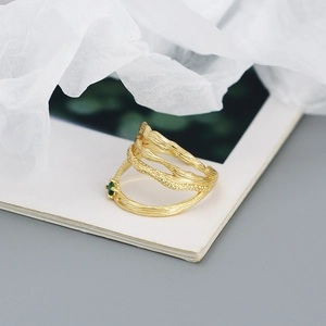 Macro detail of gold layered ring with bark texture and an inlaid green gemstone