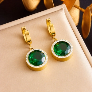 Macro detail of gold earrings featuring round green emeralds with a halo of white diamonds