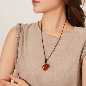 Close-up of heart-shaped red stone pendant with brown woven cord necklace on a model