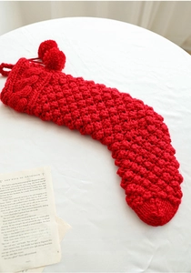 Macro detail of red cable-knit Christmas stocking with fluffy pom-poms on white background