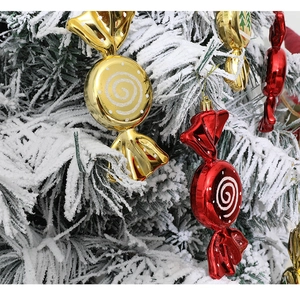 Detail of red and gold candy ornaments hanging on a snowy Christmas tree branch