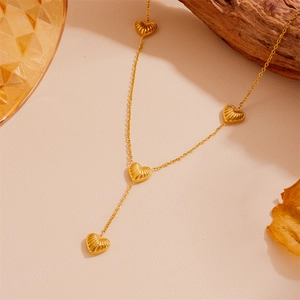 Détail du collier en acier doré avec pendentifs en forme de cœur sur un fond chaleureux