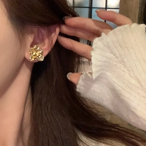Macro detail of gold flower stud earring with irregular metallic petals and small bead