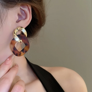 Close-up of tortoise shell pattern geometric earrings with gold link chain detailing