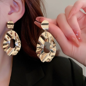 Close-up of golden irregular geometric earrings with pleated texture and hollow design
