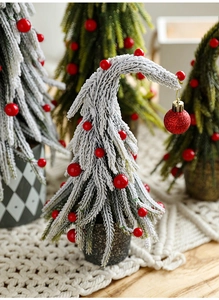 Close-up of mini snow-flocked Christmas tree with red berries and a curved top in a pot