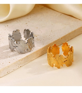 Close-up of gold and silver tropical leaf rings on stone with beige silk background