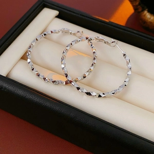 Dettaglio di orecchini a cerchio irregolari in argento con texture diamantata in scatola