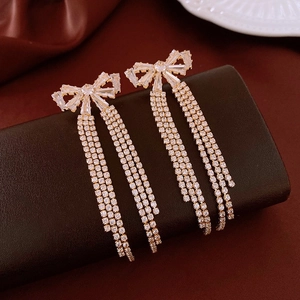 Macro detail of elegant gold bow earrings with crystal tassels on a velvet background