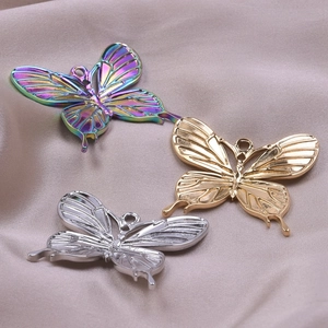 Three butterfly pendants in gold, silver, and rainbow colors on soft fabric background