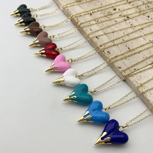 Macro detail of colorful heart pendants on gold chains over a beige stone surface