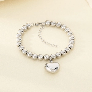 Polished silver beaded bracelet with heart pendant and lobster clasp on textured surface