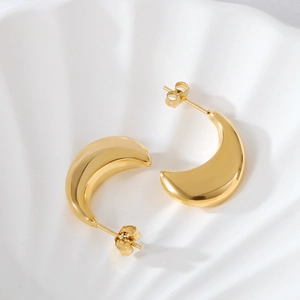 Detail of elegant gold crescent earrings with mirror finish on white shell background