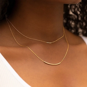 Detail einer goldenen mehrlagigen Halskette mit Staban hänger und kleiner Perle am Model